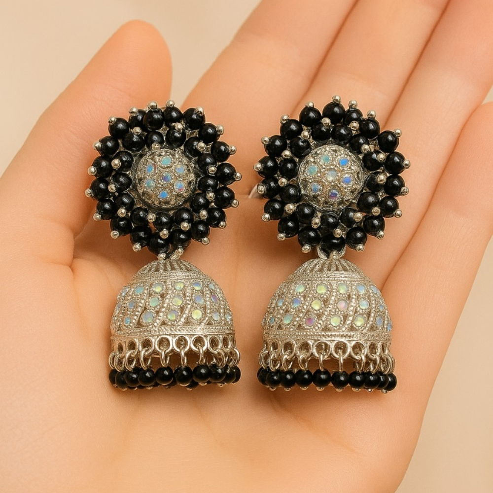 Pair of ornate earrings with black beads held in a hand against a beige background