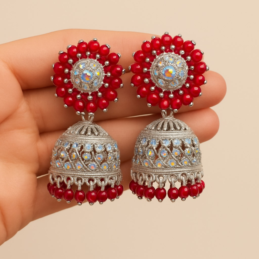 Red and silver earrings held in a hand against a beige background