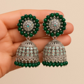 Pair of green and silver earrings held in a hand against a beige background