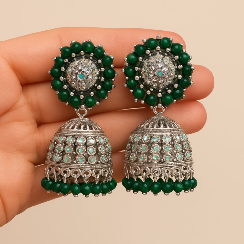 Pair of green and silver earrings held in a hand against a beige background