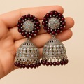 Ornate earrings with maroon beads held in a hand against a beige background