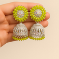 Pair of silver and green beaded earrings held between fingers against a beige background