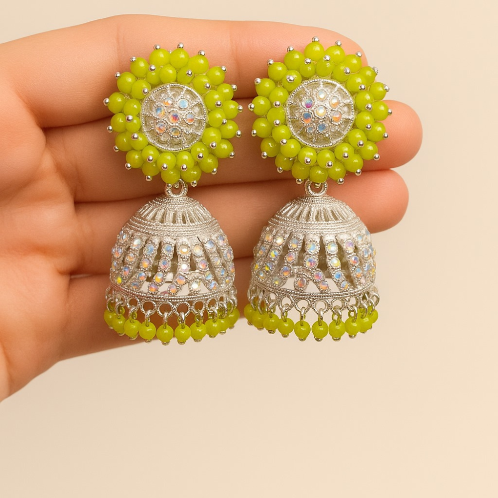 Pair of silver and green beaded earrings held between fingers against a beige background