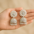 Pearl and silver earrings held in a hand against a beige background