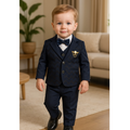 Young boy in a formal navy suit with a bow tie standing in a living room.