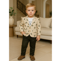 Young boy in a beige blazer with green pattern standing in a living room.